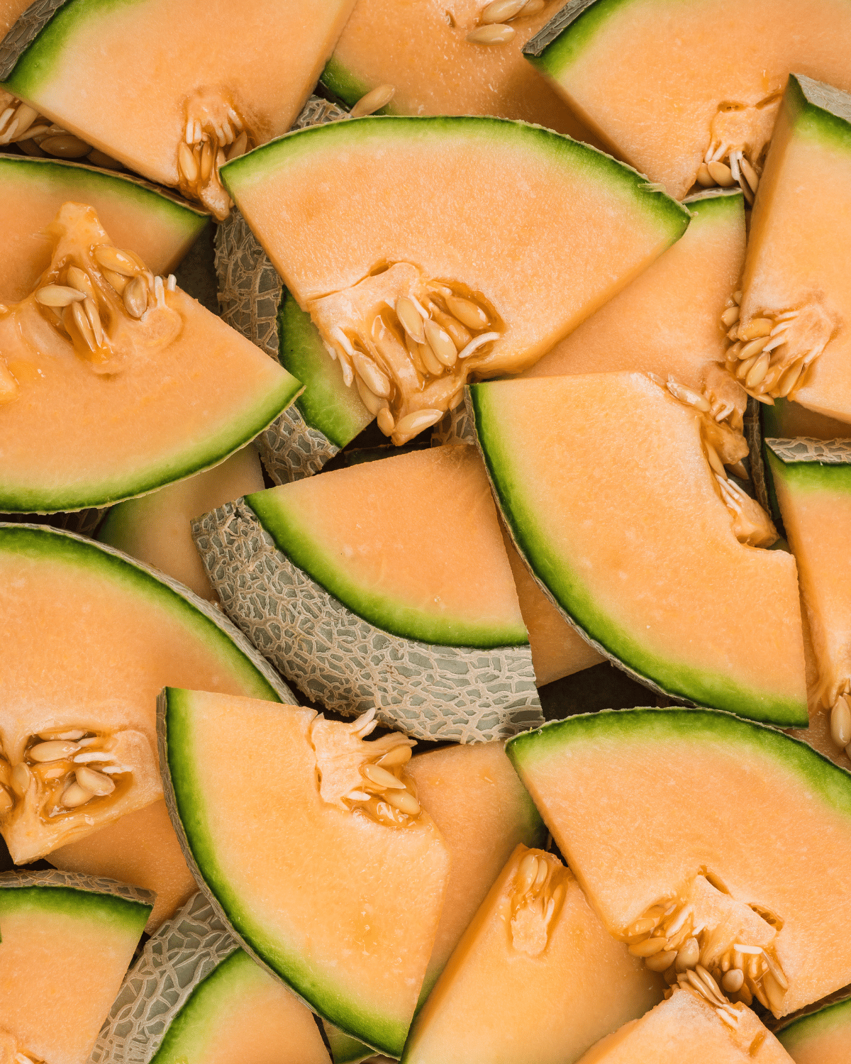 Close-up of a premium large cantaloupe showing the intricate textured webbing of the skin and the deep, salmon-colored interior of a freshly cut slices.