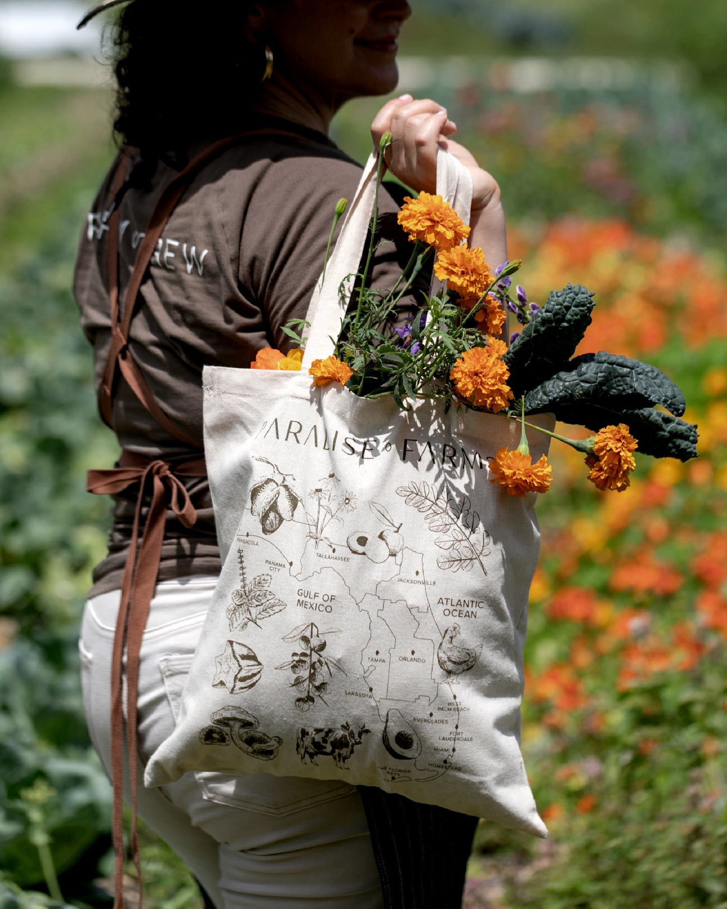 Person holding a tote bag with botanical designs and flowers in a garden setting