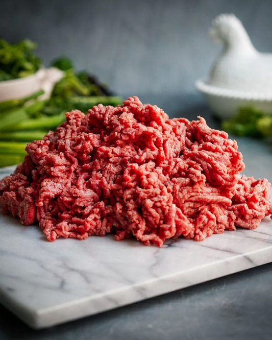 Raw ground meat on a marble slab with vegetables in the background
