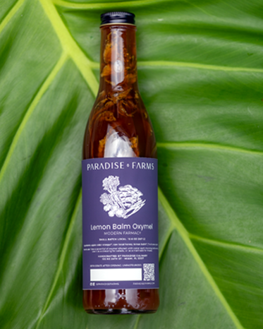 Bottle of Paradise Farms Lemon Balm Oxymel on a large green leaf